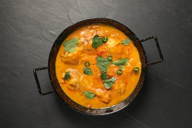 Photo of Tasty chicken curry with parsley and pepper on black textured table, top view