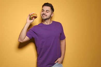 Handsome man with tasty burger on color background