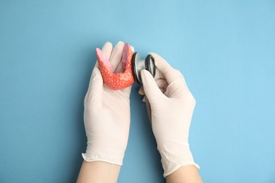 Photo of Doctor with stethoscope examining healthy thyroid on light blue background, top view