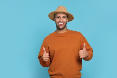 Photo of Happy African American man showing thumbs up on light blue background. Space for text