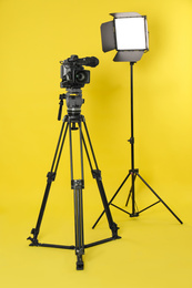 Photo of Professional video camera and lighting equipment on yellow background