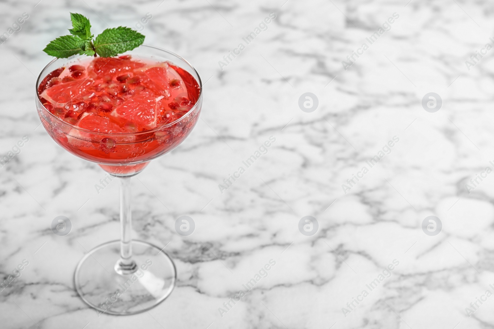 Photo of Glass of tasty refreshing cocktail with grapefruit and pomegranate on white marble table. Space for text