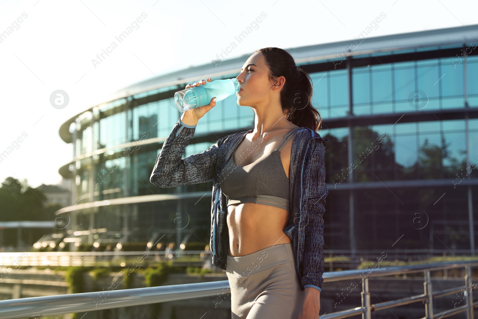 Photo of Young woman drinking water after running in city. Sports hydration
