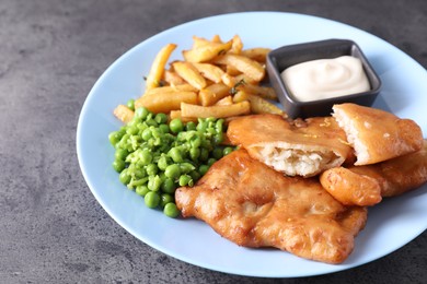 Photo of Tasty fish, chips, sauce and peas on grey table, closeup