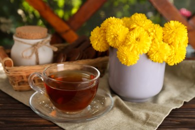 Beautiful yellow chrysanthemum flowers and cup of aromatic tea on wooden table