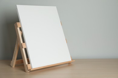 Photo of Wooden easel with blank canvas on table. Space for text