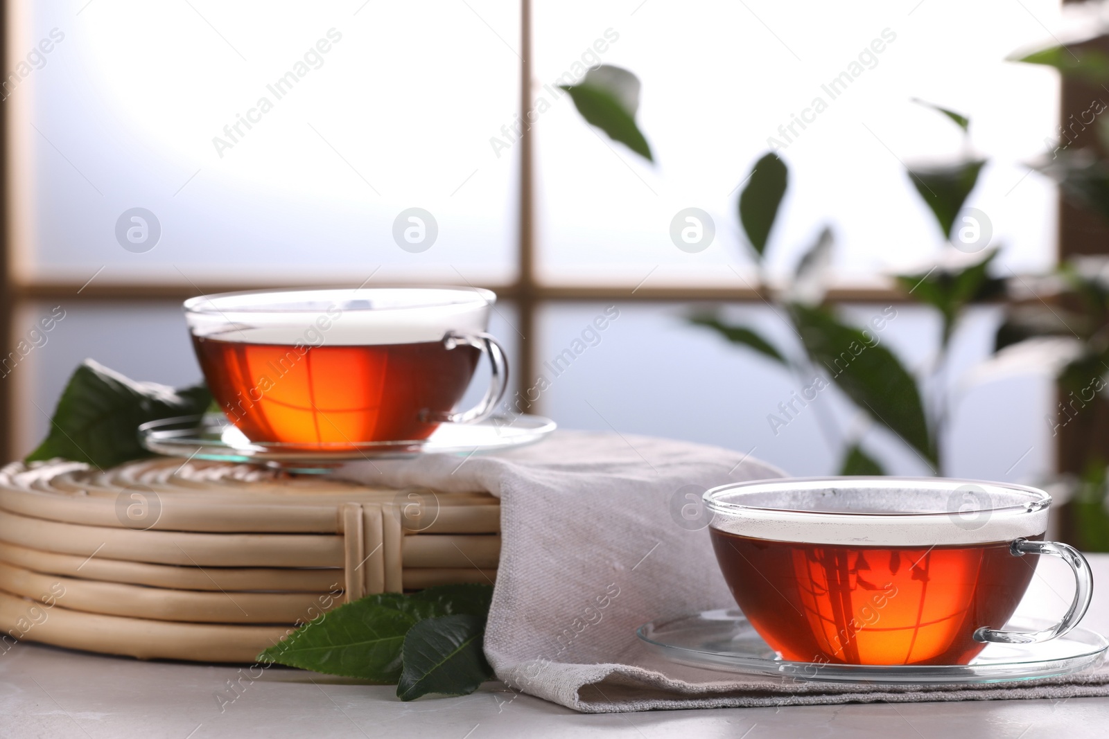 Photo of Aromatic hot tea in glass cups and green leaves on white table indoors