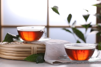 Photo of Aromatic hot tea in glass cups and green leaves on white table indoors