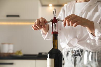 Photo of Woman opening wine bottle with corkscrew indoors, closeup. Space for text