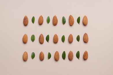 Photo of Delicious almonds and fresh leaves on beige background, flat lay