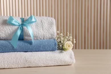 Photo of Soft towels, gypsophila and eustoma flowers on light wooden table, space for text