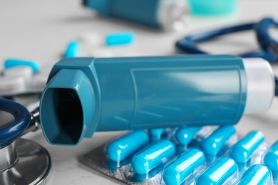 Asthma inhaler, stethoscope and pills on table, closeup