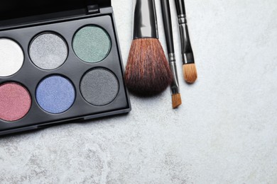 Beautiful eye shadow palette and brushes on grey table, flat lay. Space for text