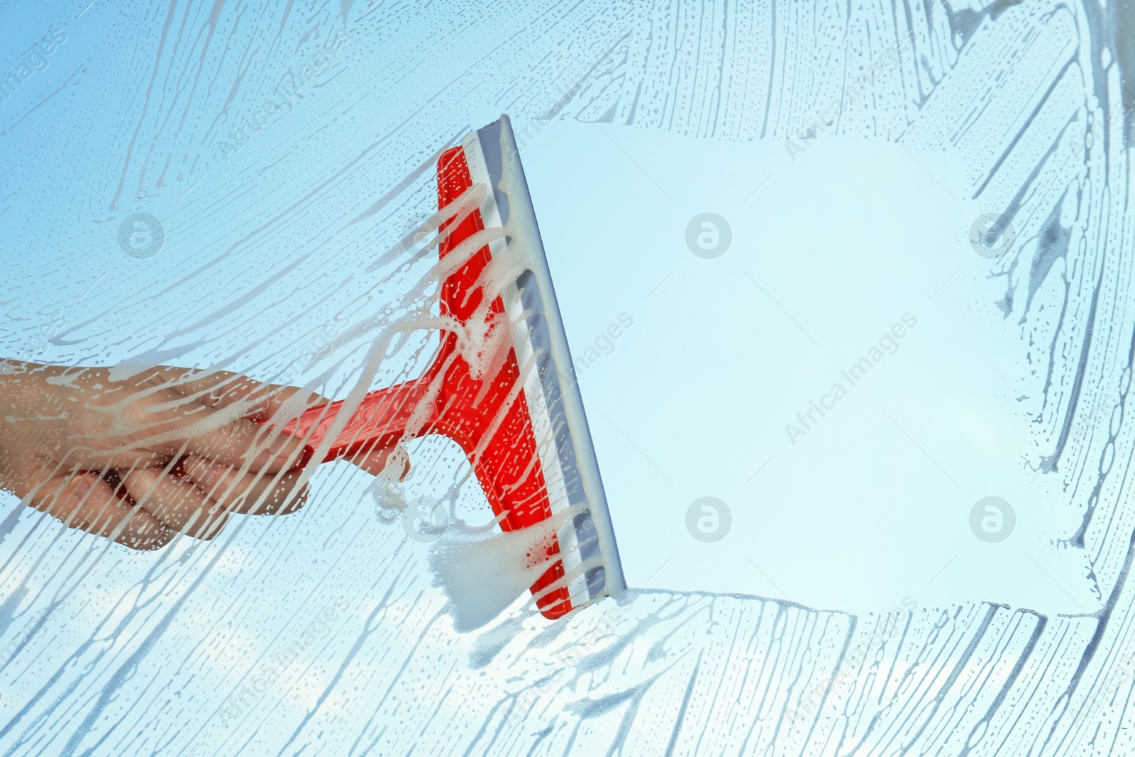 Photo of Woman cleaning window with squeegee on spring day, closeup