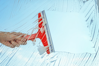 Photo of Woman cleaning window with squeegee on spring day, closeup