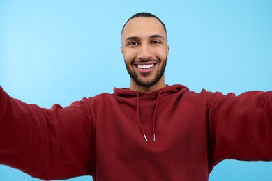 Photo of Smiling young man taking selfie on light blue background