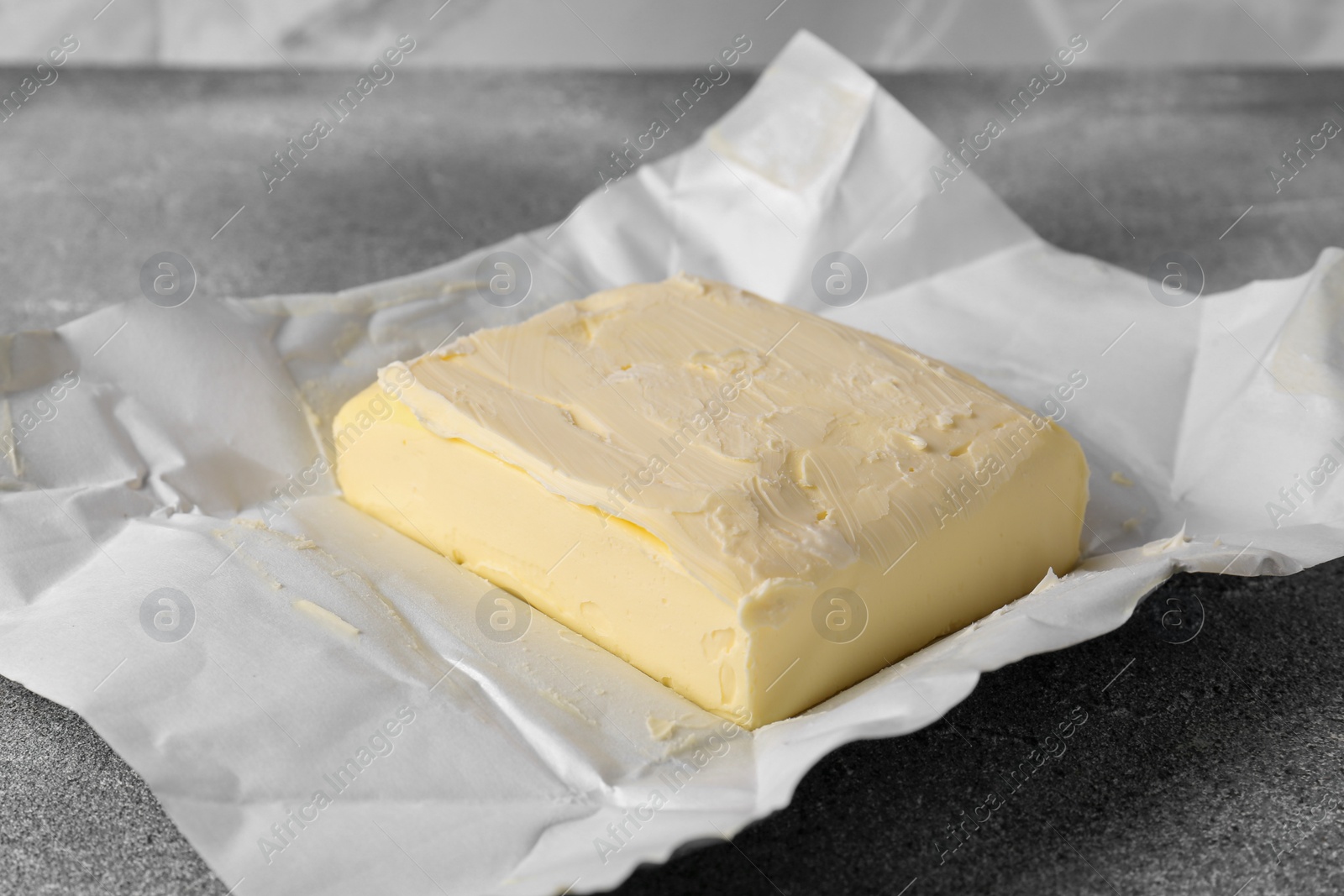 Photo of Paper wrap with tasty homemade butter on grey table