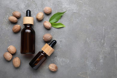 Photo of Bottles of nutmeg oil and nuts on grey table, flat lay. Space for text