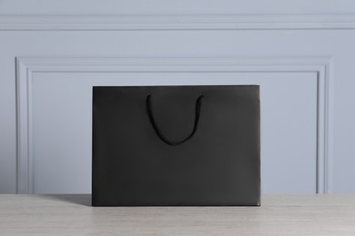 Photo of Black paper bag on wooden table against light grey wall