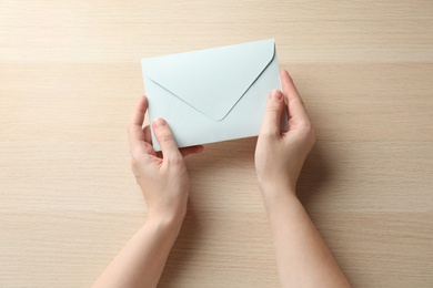 Photo of Woman with white paper envelope at wooden table, top view