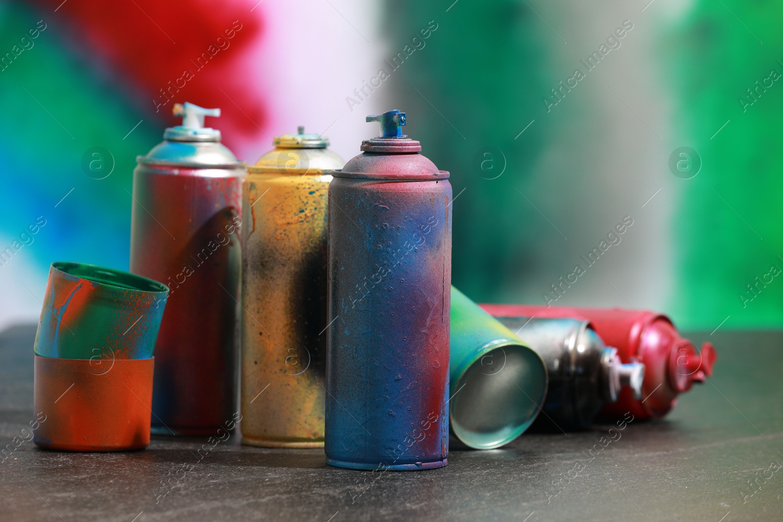 Photo of Many spray paint cans on gray surface against color background