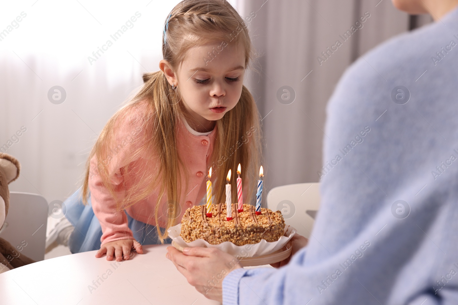 Photo of Birthday celebration. Mother holding tasty cake with burning candles near her daughter indoors