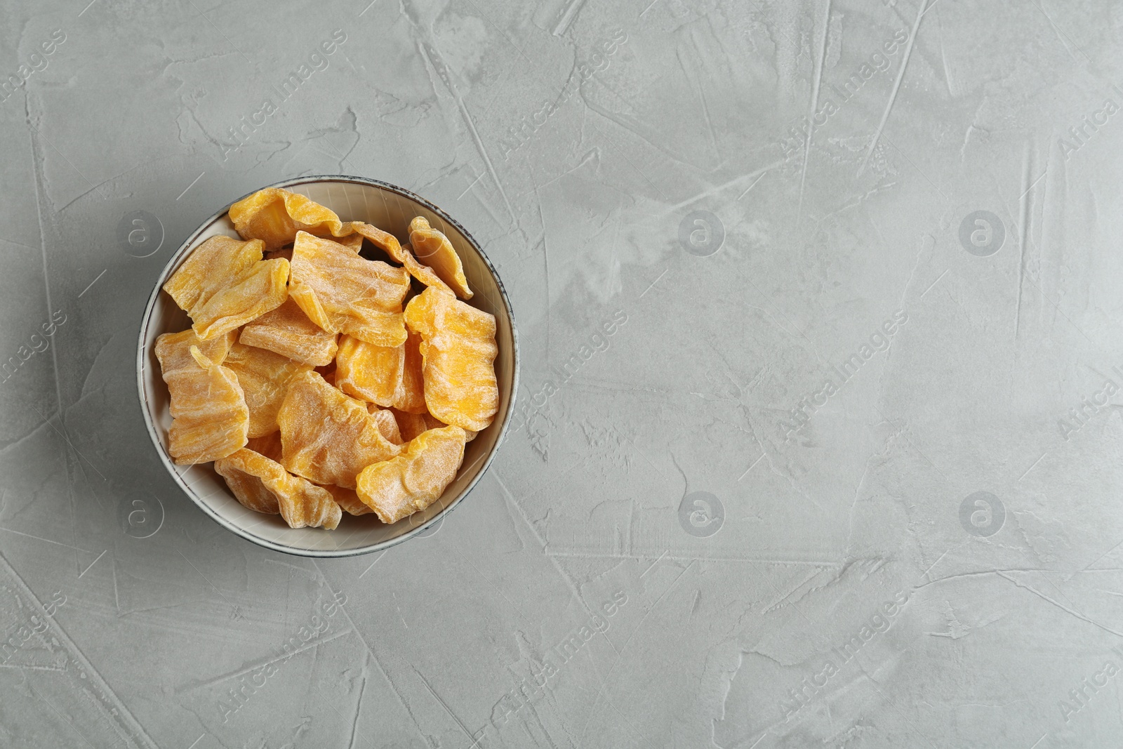 Photo of Delicious dried jackfruit slices in bowl on grey table, top view. Space for text