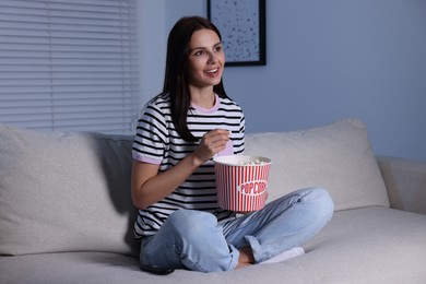Photo of Happy woman with popcorn bucket watching TV at home in evening