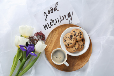 Photo of Delicious coffee, cookies, flowers and GOOD MORNING wish on white cloth, flat lay