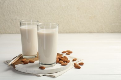 Photo of Glasses of almond milk and almonds on white wooden table, space for text