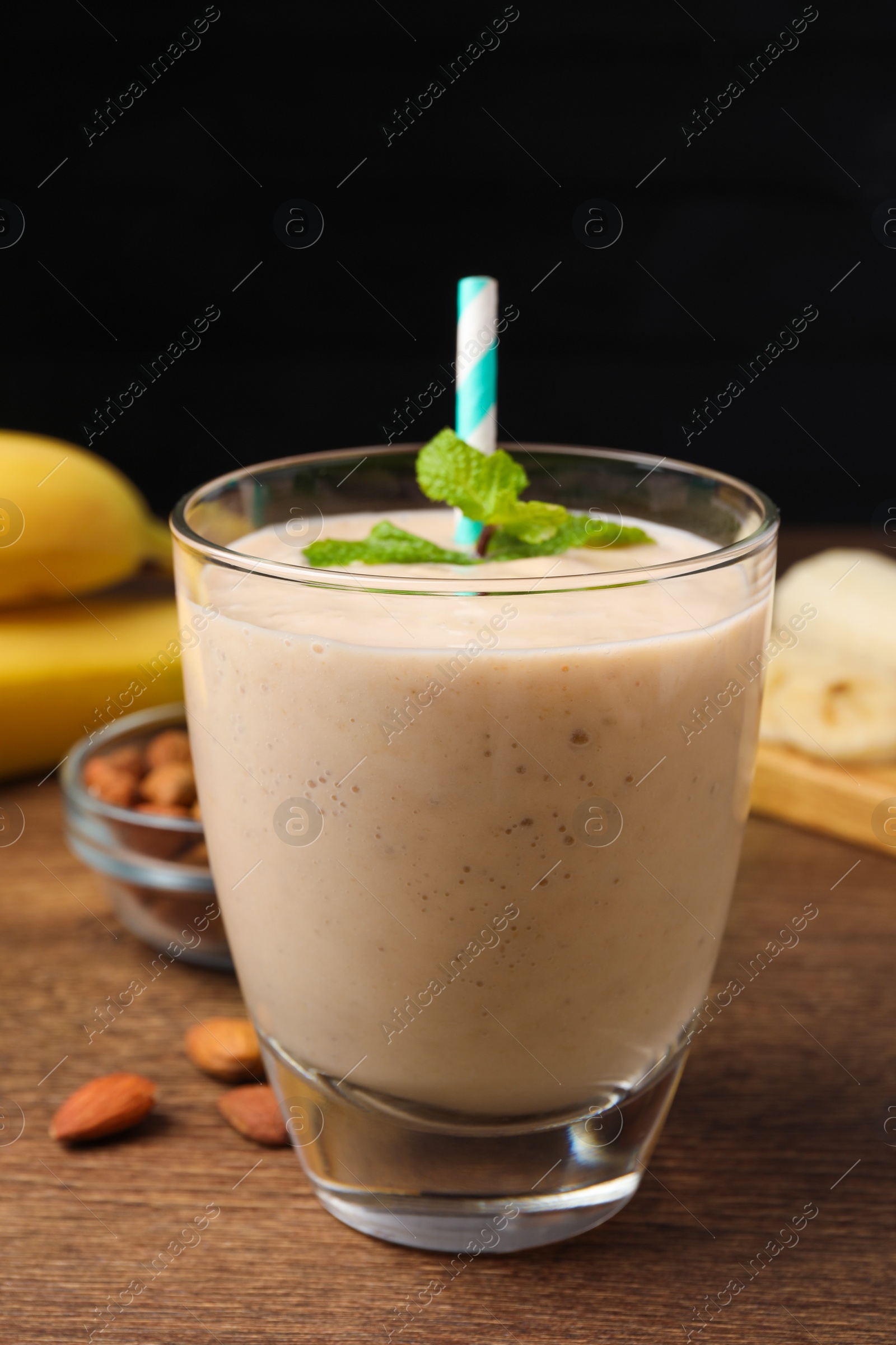 Photo of Glass with banana smoothie and mint on wooden table against black background