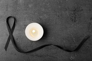 Photo of Black ribbon and candle on grey background, top view. Funeral symbols