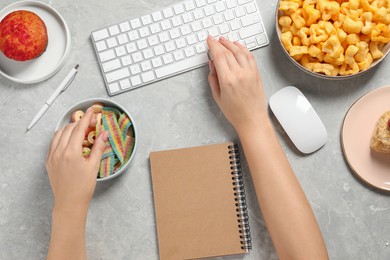 Photo of Bad habits. Woman eating different snacks while working on computer at grey marble table, top view