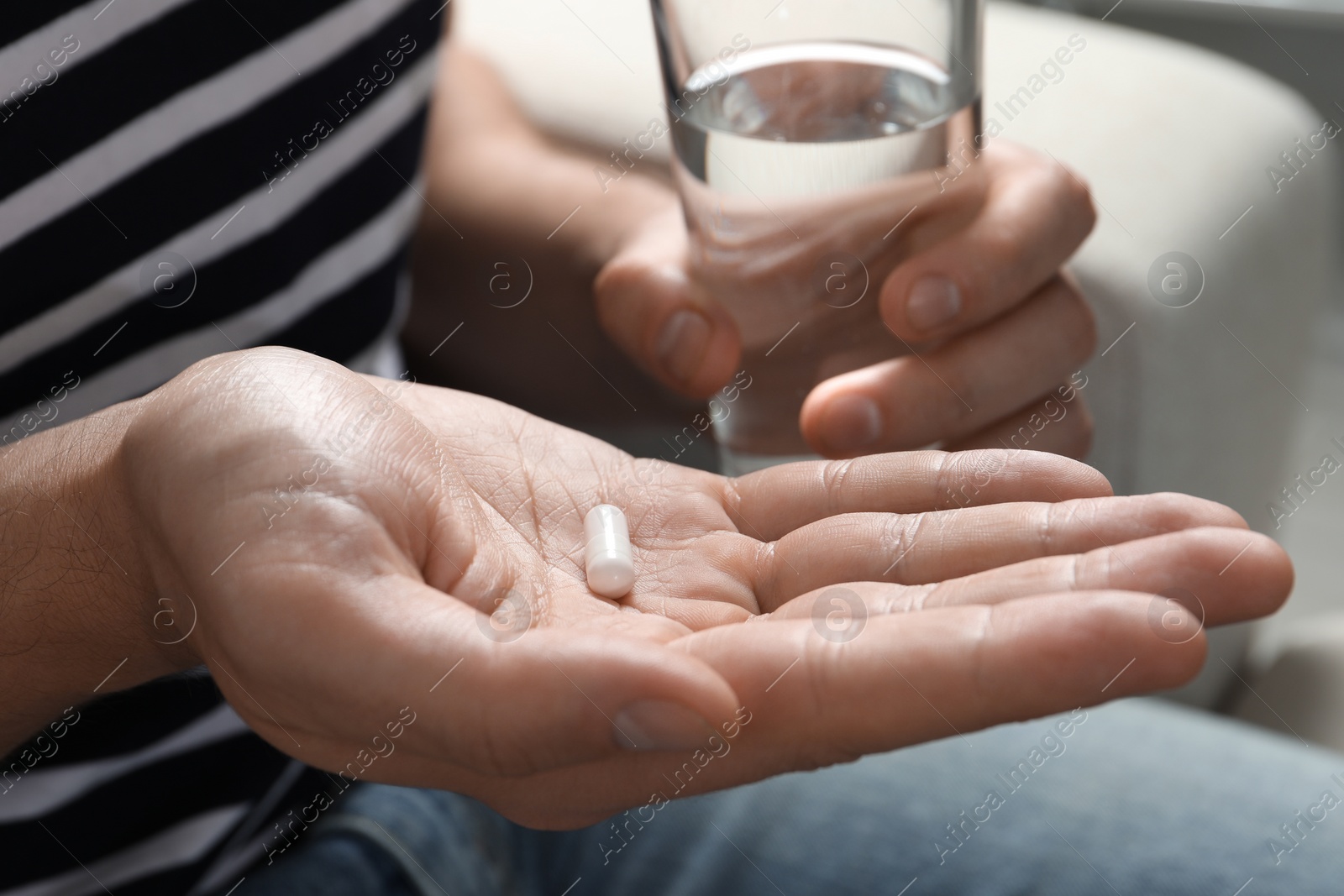 Photo of Man with glass of water and pill on blurred background, closeup