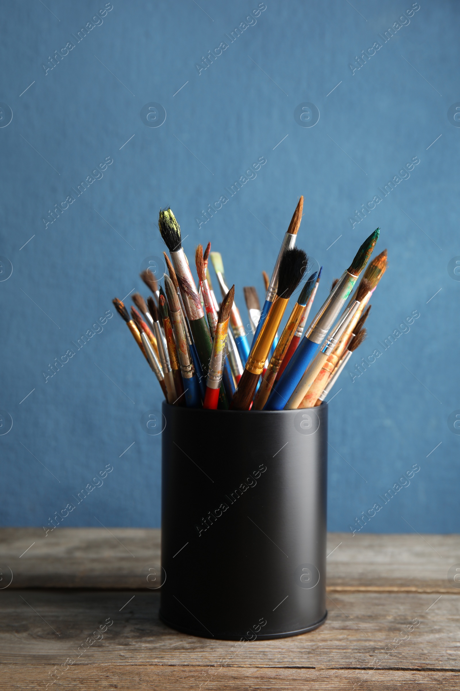 Photo of Holder with paint brushes on table against color background