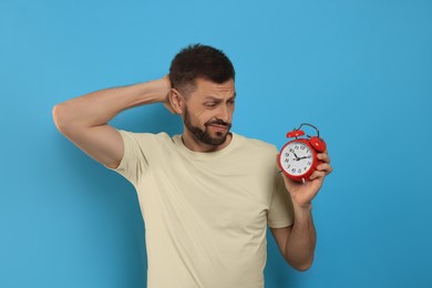 Emotional man with alarm clock on light blue background. Being late concept