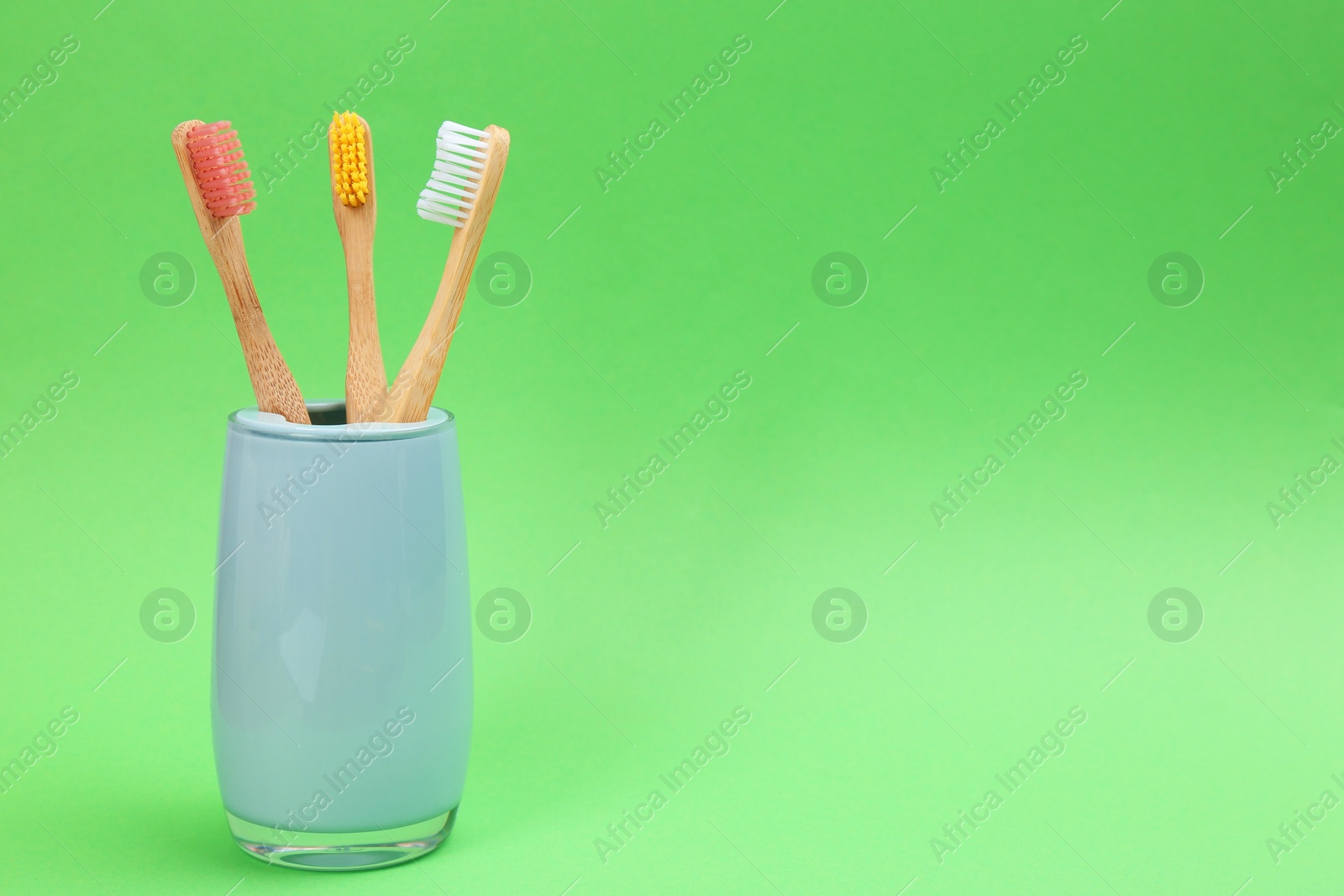 Photo of Bamboo toothbrushes in holder on green background, space for text