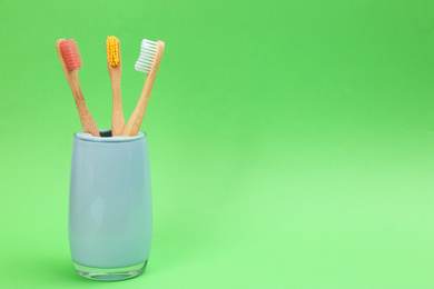 Photo of Bamboo toothbrushes in holder on green background, space for text