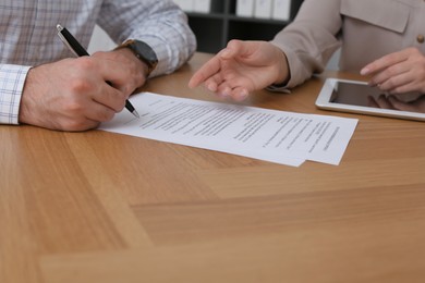 Businesspeople signing contract at wooden table, closeup of hands