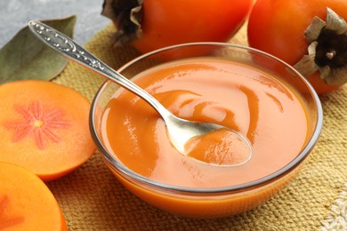 Photo of Delicious persimmon jam in glass bowl served on table, closeup