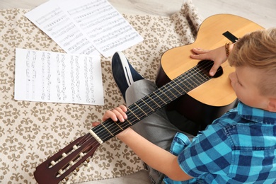 Little boy playing guitar on floor in room