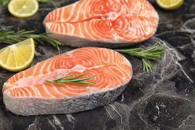 Photo of Fresh raw salmon, rosemary and lemon on black marble table. Fish delicacy