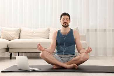 Photo of Man in sportswear meditating near laptop at home. Harmony and zen