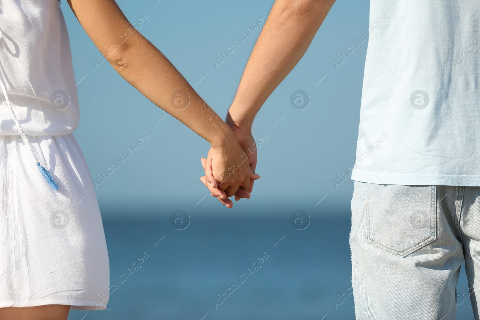 Photo of Happy young couple holding hands at beach on sunny day, closeup