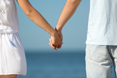 Happy young couple holding hands at beach on sunny day, closeup