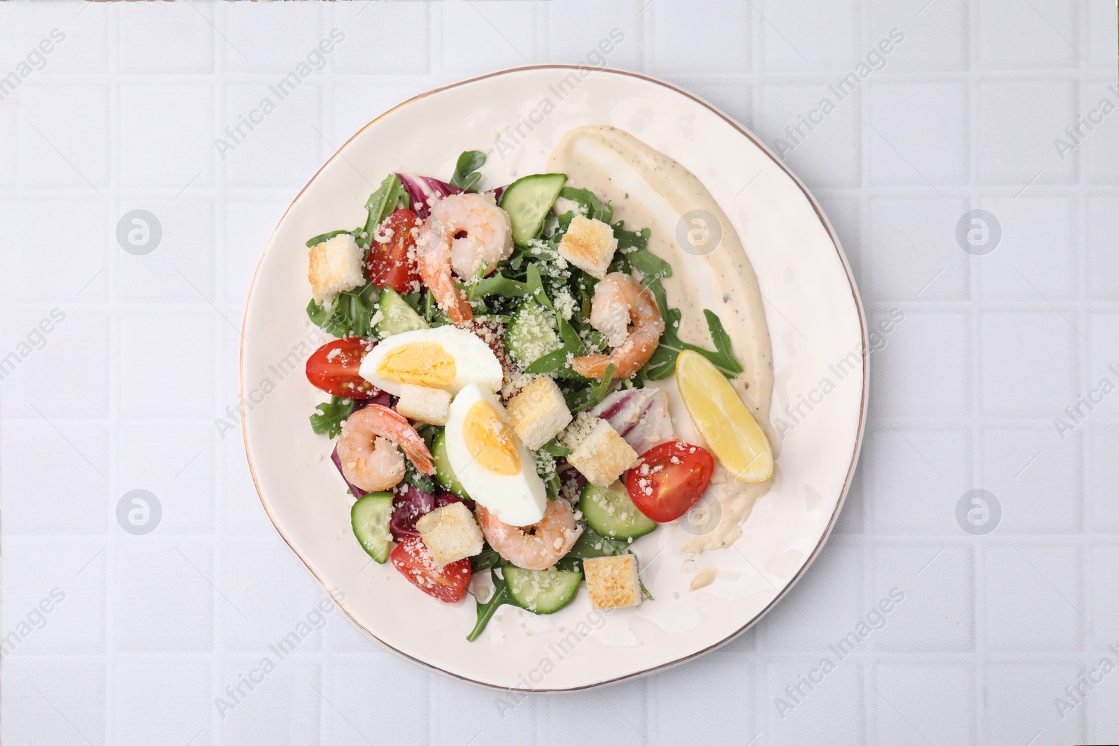 Photo of Delicious Caesar salad with shrimps on white tiled table, top view