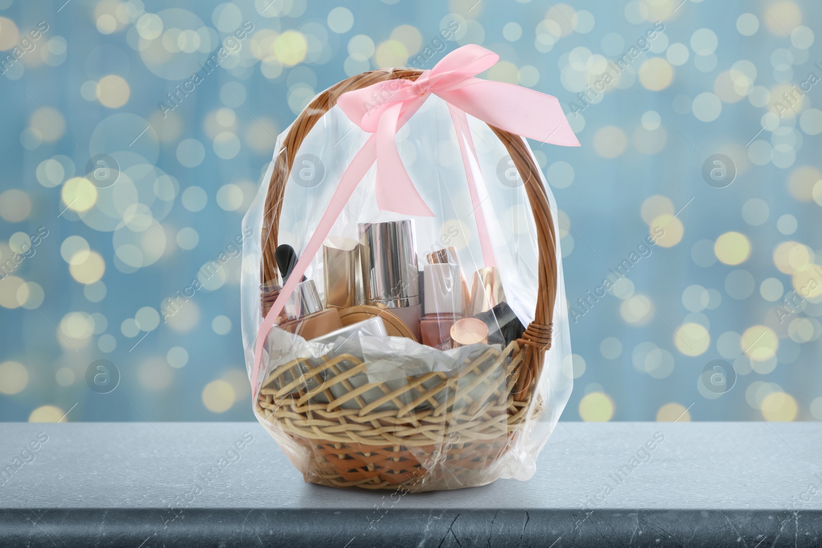 Image of Wicker basket full of cosmetic products on table against blurred festive lights 