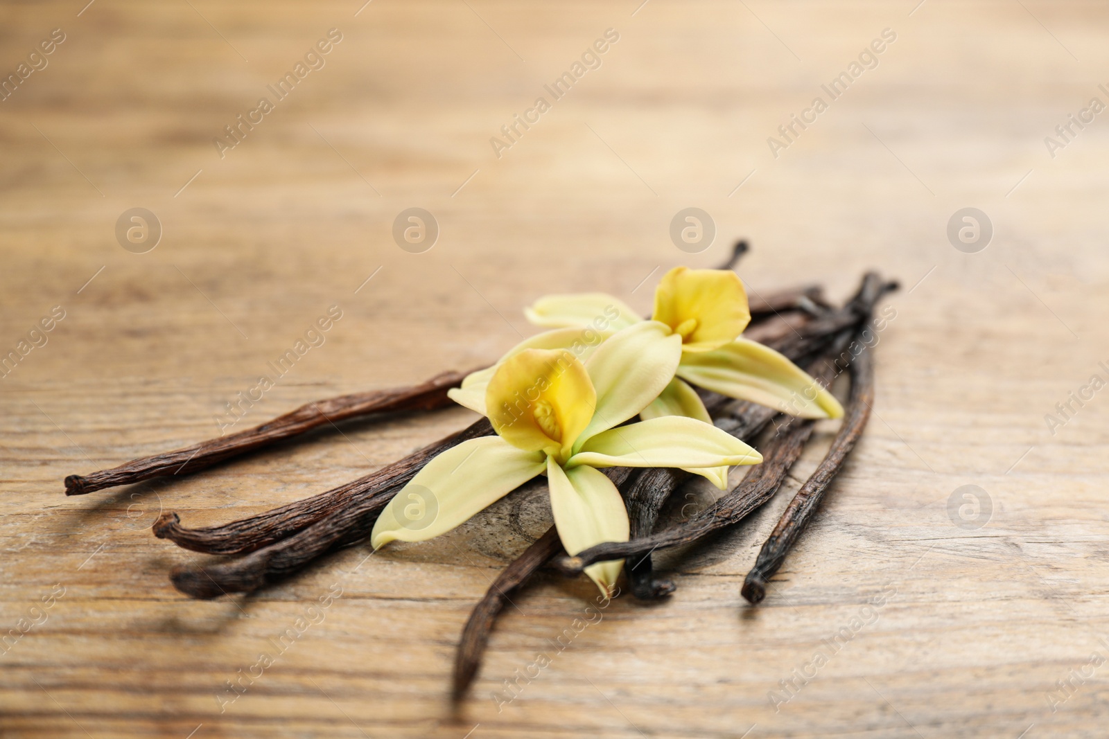 Photo of Beautiful vanilla flowers and sticks on wooden table, closeup