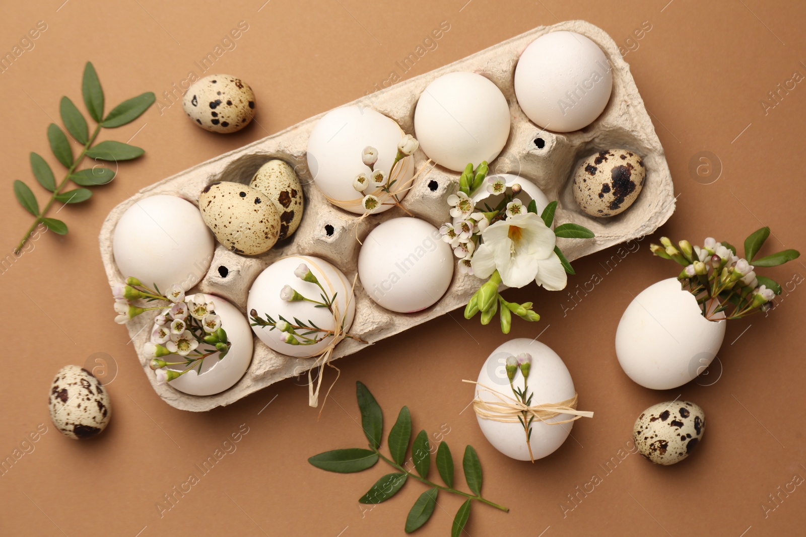 Photo of Festive composition with eggs and floral decor on brown background, flat lay. Happy Easter