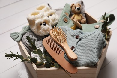 Photo of Wooden crate with children's clothes, shoes, toy, pacifier, hair brush and comb on white table